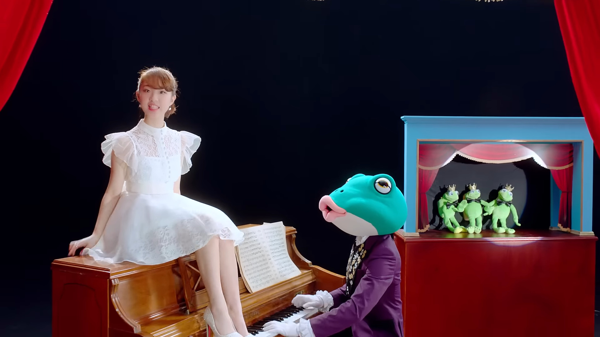 Yeojin sitting on a piano being played by the frog, next to a frog puppet show.